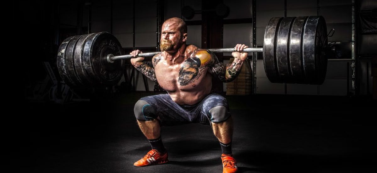 Muscular man lifting heavy weights during an intense squat session inside a gym.