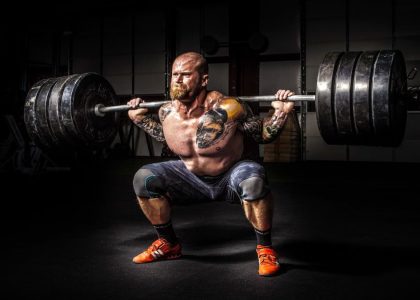 Muscular man lifting heavy weights during an intense squat session inside a gym.